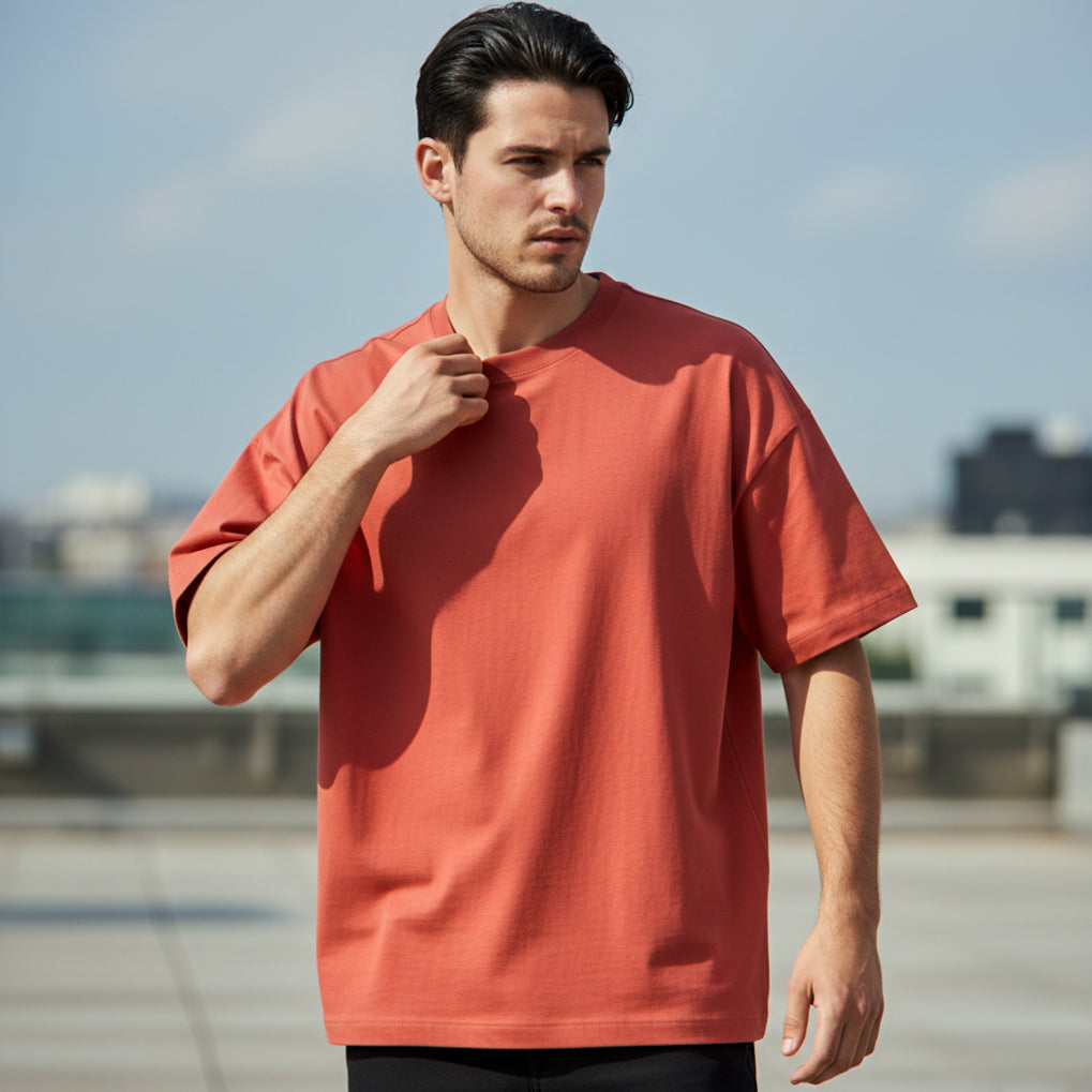 Male model wearing a plain Brick Red Premium Oversized T-shirt standing outdoors with a blurred background.