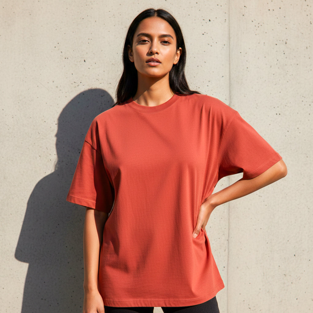 Woman model wearing a plain Brick Red Premium Oversized T-shirt against a concrete wall.