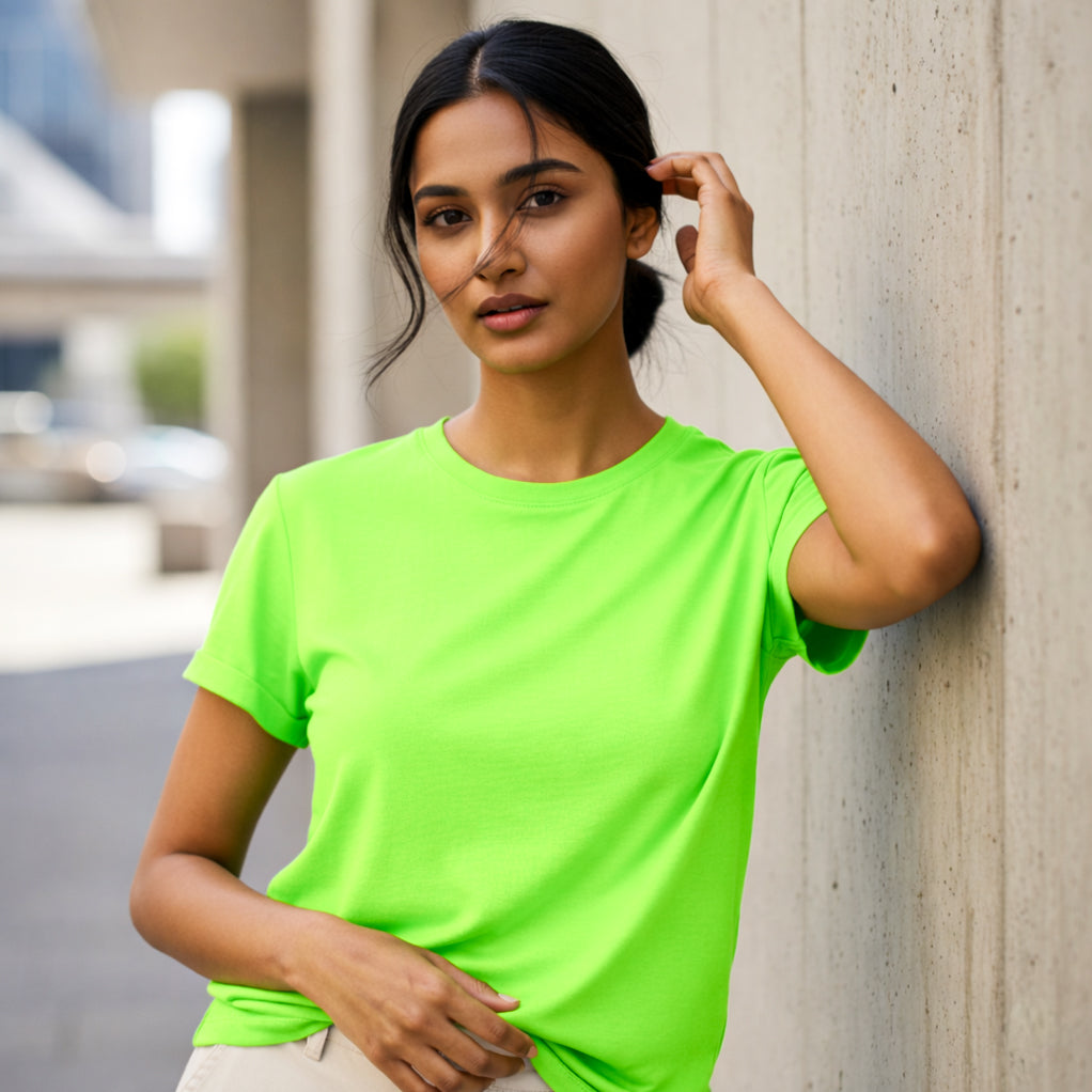 Young woman model wearing a bright green t-shirt leaning against a wall outdoors. Plain Liril Green Women's T-shirt by Paryatak Travel Shop.