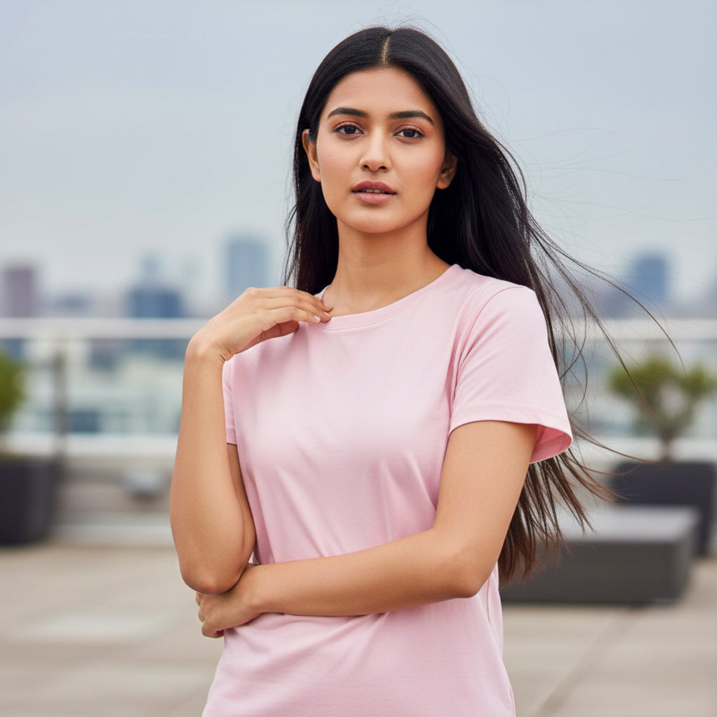 Female model wearing a pink t-shirt on a rooftop with a cityscape background. Plain Light Pink Women's T-shirt by Paryatak Travel Shop.