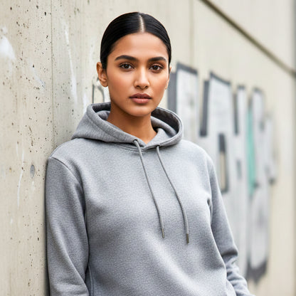 Woman model wearing a melange grey hoodie leaning against a concrete wall. Plain Melange Grey Hoodie by Paryatak Travel Shop.