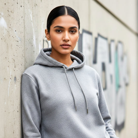 Woman model wearing a melange grey hoodie leaning against a concrete wall. Plain Melange Grey Hoodie by Paryatak Travel Shop.
