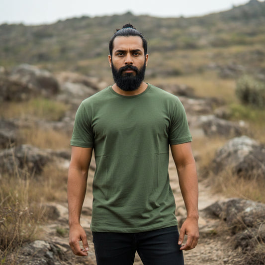 Male model wearing an olive green t-shirt standing in a rocky, outdoor landscape. Plain Olive Green Men's T-shirt by Paryatak Travel Shop.