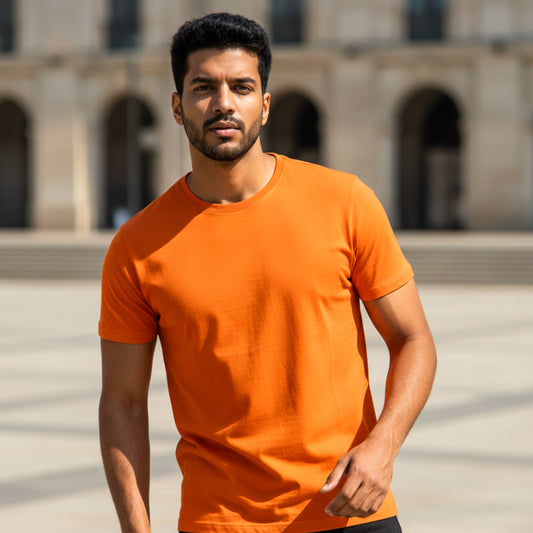 Male model wearing an orange t-shirt standing in front of a building with arches. Plain Orange Men's T-shirt by Paryatak Travel Shop.