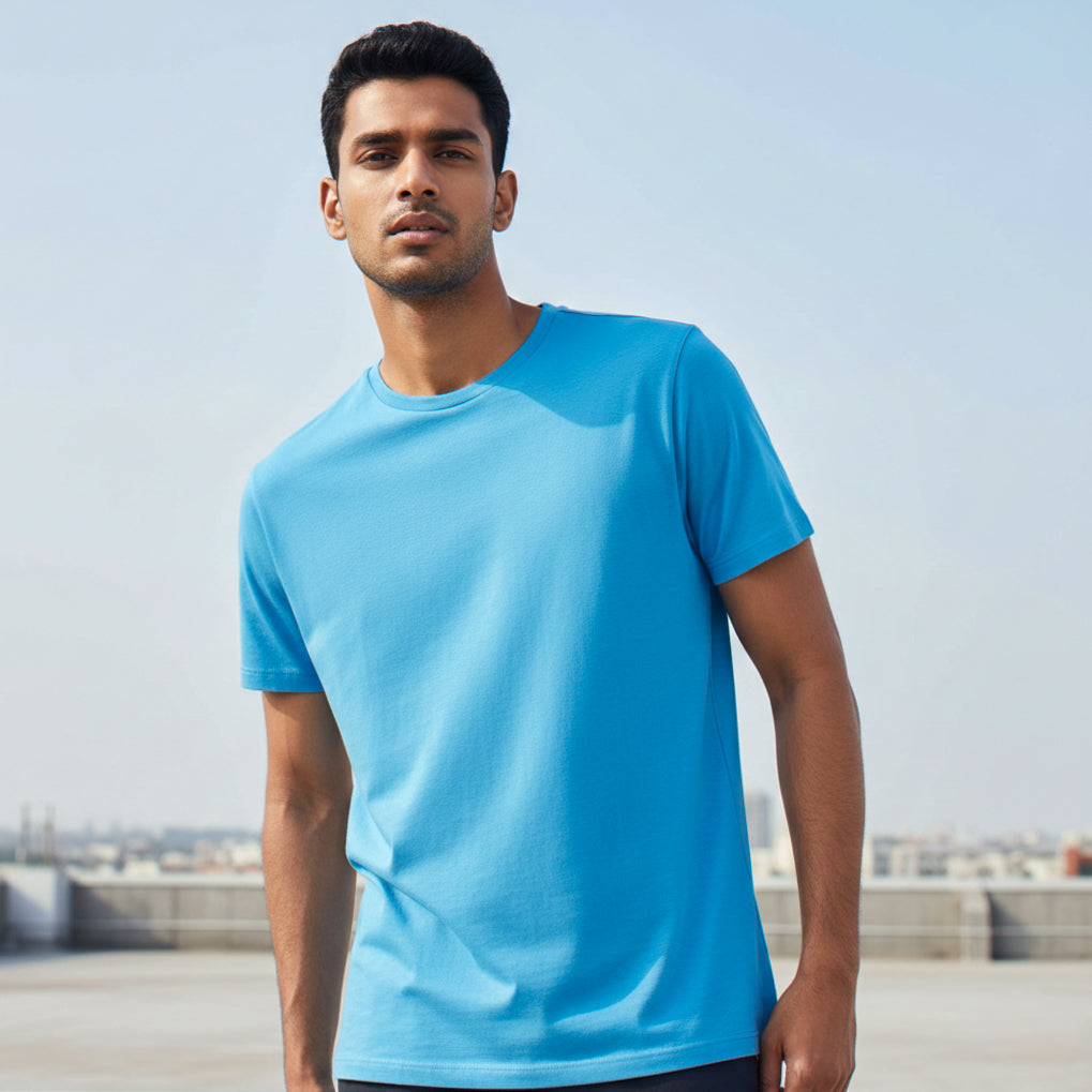 Male model wearing a blue t-shirt standing outdoors with a clear sky background. Plain Sky Blue Men's T-shirt by Paryatak Travel Shop.