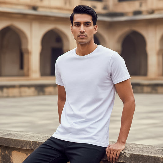 Male model wearing a white t-shirt sitting on a stone ledge with an architectural background. Plain White Men's T-shirt by Paryatak Travel Shop.